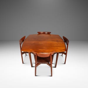May include: A mid-century modern dining set featuring a rectangular wooden table and four matching chairs. The table has a rich, warm wood tone, and a small wooden bowl sits in the center. The chairs have curved backs and angled legs.