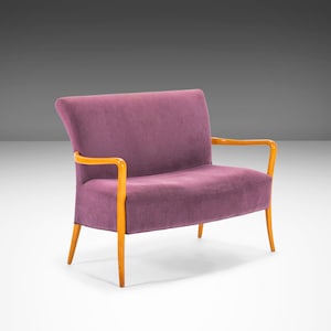 May include: A purple two-seater sofa with wooden arms and legs. The sofa is upholstered in a soft, textured fabric.
