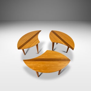 May include: Three wooden nesting tables with a light wood finish and a curved, leaf-shaped design. The tables are arranged in a circle.