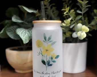 May include: A frosted glass water bottle with a bamboo lid and a straw. The bottle has a floral design with yellow flowers and green leaves. The bottle has a quote from Jeremiah 29:11, "For I know the plans I have for you," declares the Lord.