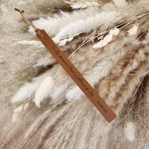 May include: A brown leather bookmark with the text "In His presence there is fullness of Joy" and "Psalm 16:11". The bookmark is attached to a bundle of dried flowers in shades of beige and brown.