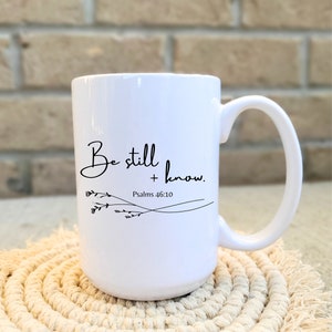 May include: White ceramic mug with a black inscription that reads "Be still and know."  The inscription is accompanied by a small floral design and the text "Psalms 46:10".