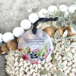 May include: A round glass ornament with a floral design and the quote "I can do all things through Christ who gives me strength. Philippians 4:13" printed on it.
