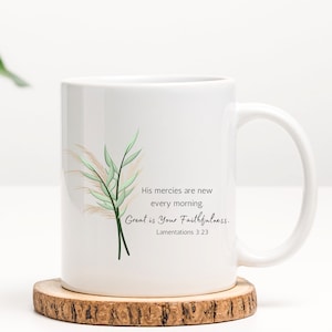 May include: White ceramic mug with a green and beige floral design. The mug has a quote that reads "His mercies are new every morning. Great is Your Faithfulness. Lamentations 3:23"