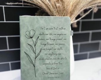 May include: Sage green journal with a floral line drawing and the text of Romans 8:38-39. The journal has a simple, elegant design, perfect for writing or note-taking. The cover features a minimalist flower illustration.