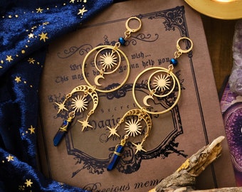 May include: Gold earrings with a sun and moon design, featuring blue crystal accents. The earrings are displayed on a book with the text "This magic box is going to help you..." and "Secret Magic".
