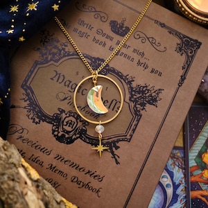 Puede incluir: Un collar de oro con un dije de luna creciente y una estrella cuelga de un libro con el texto "Este libro mágico te va a ayudar a escribir tu deseo..." y "Precious memories Note, Idea, Memo, Daybook 1981".