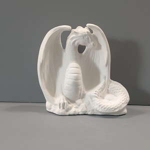 May include: White ceramic dragon figurine with wings outstretched and tail curled. The dragon is sitting on a rock base.