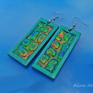 May include: A pair of iridescent green and orange rectangular earrings with a textured surface. The earrings have silver hooks.