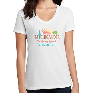 May include: White V-neck t-shirt with a colorful graphic. The graphic includes the text "MICHIGANDER" above "On Spring Break", a sun, palm tree, and waves. The shirt is short-sleeved.