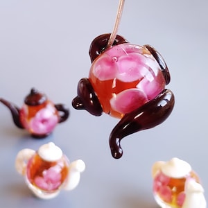 Peut inclure: Quatre théières miniatures en verre avec des motifs floraux roses à l'intérieur. Les théières sont brunes et ont une finition brillante. Une théière est suspendue dans les airs.