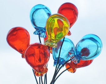 Könnte beinhalten: Ein Bündel bunter Glasballons, die mit schwarzen Schnüren zusammengebunden sind. Die Ballons sind rot, blau und gelb.