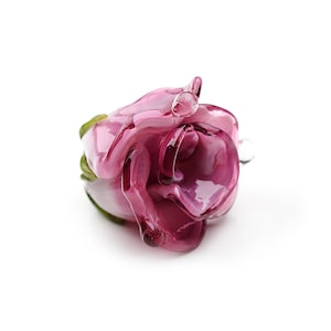 May include: A glass rose bead in shades of pink and purple. The rose is detailed with a green stem and leaves.