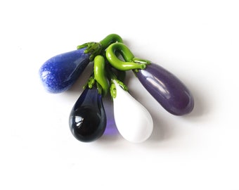 Puede incluir: Cuatro berenjenas de vidrio en diferentes colores: azul, negro, blanco y morado. Las berenjenas están unidas entre sí con tallos verdes.