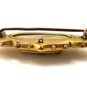 May include: A gold-toned brooch with a scalloped edge and a round, white cameo in the center. The brooch has a pin and catch closure.