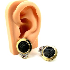 May include: A pair of gold earrings with a black cameo set in a gold frame. Each earring has a small red stone on the bottom.