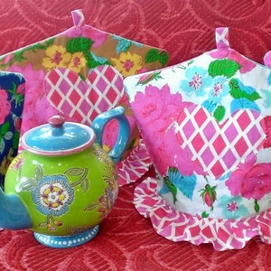 May include: Four colorful tea cozy covers with pink and white hearts and floral patterns. The covers are made of fabric and have a ruffled edge. A green and gold teapot is in the center of the image.