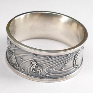 Puede incluir: Un anillo de plata con un diseño intrincado de planetas y estrellas. El anillo es ancho y tiene un acabado pulido.