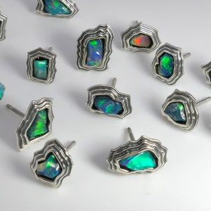 May include: A collection of 12 silver earrings with iridescent opal stones. Each earring features a unique, textured, silver setting.