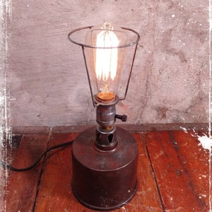 May include: A vintage-style table lamp with a metal base and a wire cage shade. The lamp is lit with a clear Edison bulb.