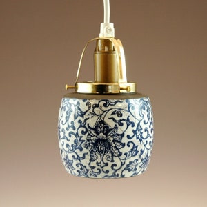 Peut inclure: Un luminaire suspendu en céramique blanche avec un motif floral bleu et blanc. Le luminaire est doté d'un cadre en métal doré et d'un cordon blanc.