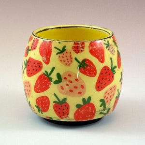 May include: A yellow ceramic bowl with a black base, decorated with a pattern of red and pink strawberries with green stems. The inside of the bowl is yellow.