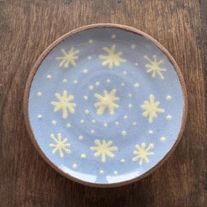 Könnte beinhalten: Ein hellblauer Keramikteller mit weißem Rand und einem Muster aus weißen Sternen und Punkten.