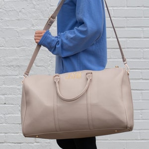 a woman carrying a beige purse in front of a white brick wall, Niagara font option