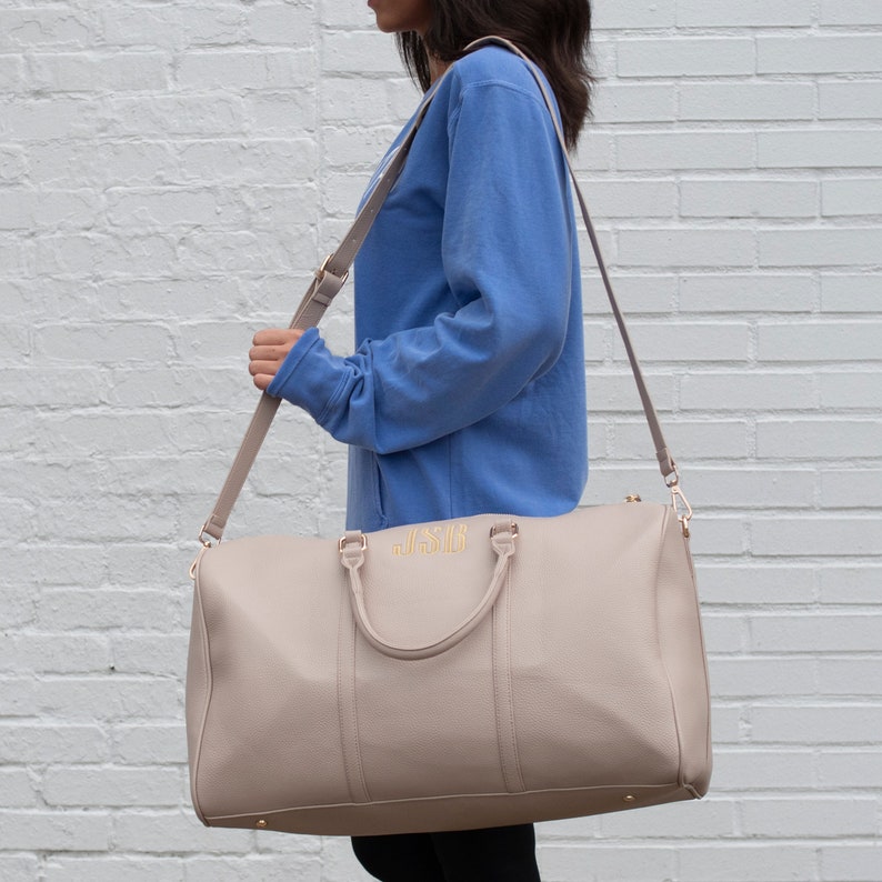 a woman carrying a beige purse in front of a white brick wall, Niagara font option