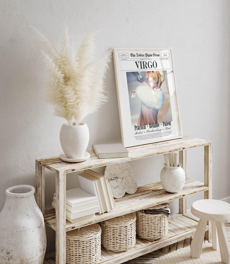 Op de afbeelding: Een rustieke houten plank toont een ingelijste "Virgo" dierenriemteken print, een witte vaas met pampasgras, boeken en decoratieve manden. De print toont een vrouw met een bontstola. Een kleine kruk en een grote witte vaas zijn ook zichtbaar.