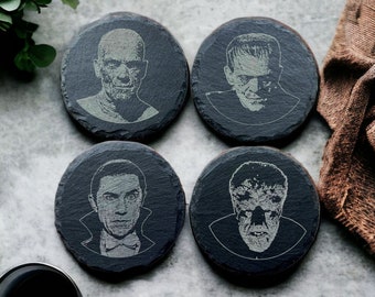 May include: Set of four black slate coasters featuring classic horror movie characters. Each coaster has a different character: Frankenstein, Dracula, the Wolfman, and the Creature from the Black Lagoon.