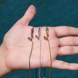 May include: Three silver chains with adjustable clasps and small beads. The chains are on a hand, with the clasps facing the camera.