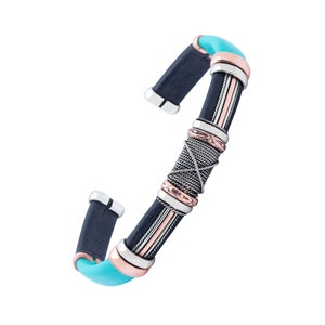 Puede incluir: Un brazalete de cuero negro con detalles plateados y cobrizos. El brazalete tiene una incrustaci&oacute;n turquesa y un dise&ntilde;o trenzado.