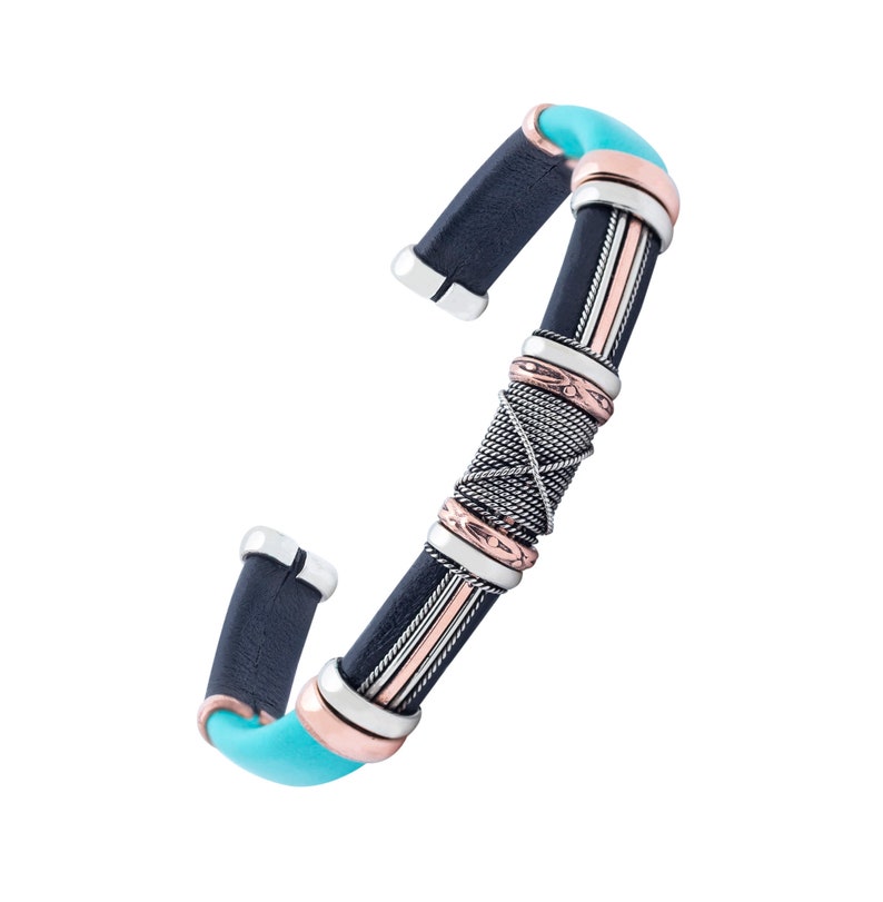Puede incluir: Un brazalete de cuero negro con detalles plateados y cobrizos. El brazalete tiene una incrustaci&oacute;n turquesa y un dise&ntilde;o trenzado.