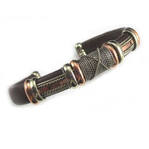 Puede incluir: Un brazalete de cuero marr&oacute;n con detalles met&aacute;licos de cobre y plata. Los detalles met&aacute;licos est&aacute;n entrelazados en un patr&oacute;n decorativo.