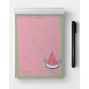 May include: A notepad with a pink interior and a green border, featuring a watermelon character illustration. The notepad has the word "notes" at the top and is accompanied by a black pen. The illustration includes the text "Richard darani illustration".