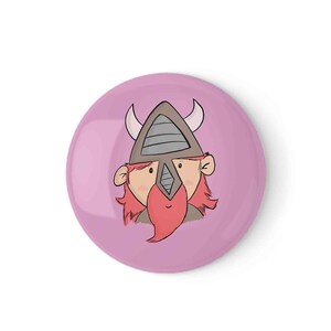 Puede incluir: Un plato decorativo redondo rosa con un diseño de vikingo de dibujos animados. El vikingo tiene un casco marrón con cuernos, una barba roja y pelo rojo. El plato es de color rosa claro liso.