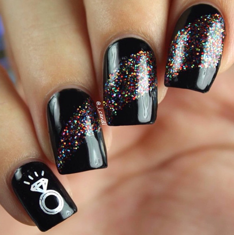 May include: Close-up of black nail polish with a glitter design. The design features a diagonal line of multi-colored glitter on each nail. One nail has a white ring with a diamond design.