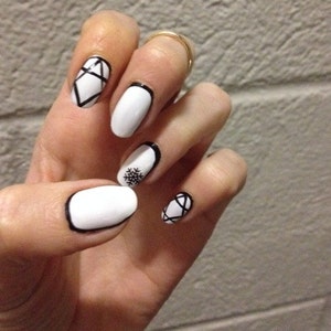 May include: White oval-shaped fingernails with black geometric designs. One nail features a snowflake design.