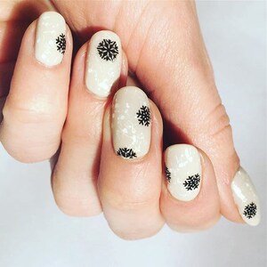 May include: Close-up of a hand with nude-colored nail polish and black snowflake nail art.