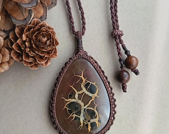 May include: A teardrop-shaped pendant featuring a brown stone with a webbed, golden-yellow crackle pattern. The stone is encased in dark brown macrame cord, which continues as an adjustable necklace cord finished with two small, round wooden beads.