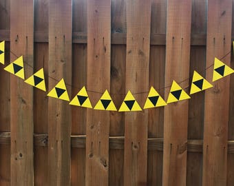 May include: A yellow and black triangle banner with a repeating pattern. The banner is strung across a wooden fence.