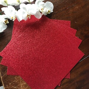 May include: A stack of red glitter paper sheets. The paper has a fine glitter finish and is perfect for crafting projects.