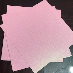 May include: Three sheets of pink glitter paper stacked on top of each other. The paper has a subtle iridescent shimmer.