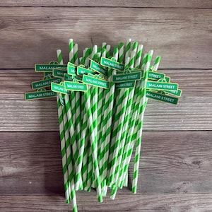 May include: A bundle of green and white striped paper straws, each adorned with a small sign that reads "MALANI STREET" in white text on a green background. The straws are arranged against a wooden background.