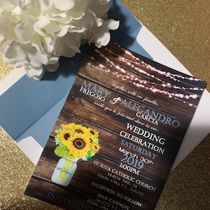 May include: Rustic wedding invitation with a wood background and string lights. The invitation features sunflowers in a mason jar with the text "Wedding" on it. The text on the invitation reads "Mary Fregoso & Alejandro Garcia Wedding Celebration Saturday March 30th 2019 1:00PM St. Rita Catholic Church 14404 14th St Dade City, FL 33523 Reception to Follow Dan Cannon 36722 FL-52 Dade City, FL 33525 Invitation Required".