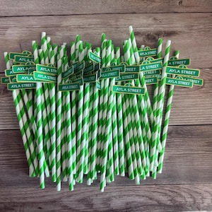 May include: A bundle of green and white striped paper straws with small green signs that read "AYLA STREET". The straws are arranged on a wooden surface.