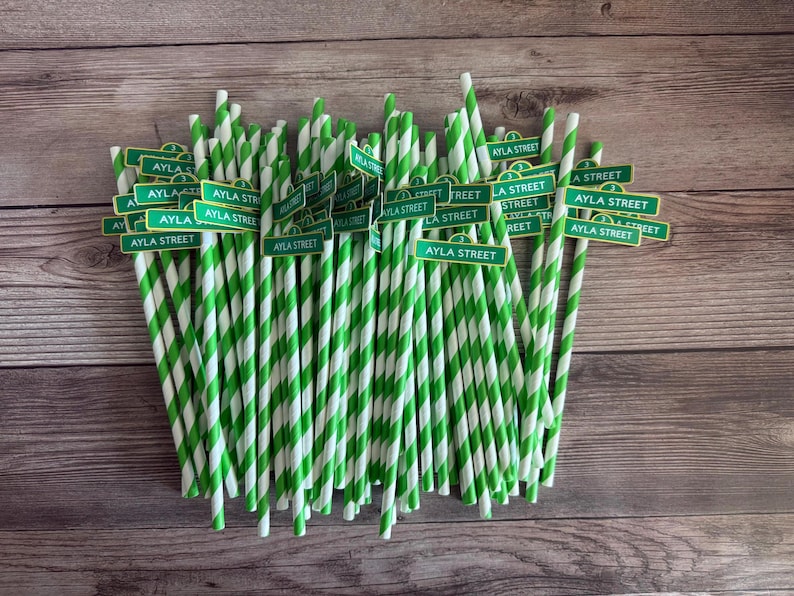 May include: A bundle of green and white striped paper straws with small green signs that read "AYLA STREET". The straws are arranged on a wooden surface.