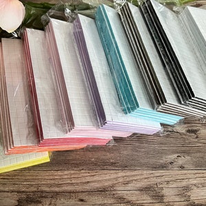 May include: A variety pack of adhesive foam squares in different colors, including yellow, orange, red, pink, purple, blue, green, black, and white. The squares are packaged in clear plastic and are stacked on a wooden surface.