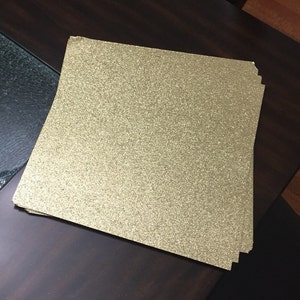 May include: A stack of gold glitter cardstock paper. The paper is textured with a fine glitter finish.